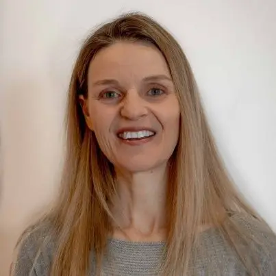 A woman with long blonde hair and a grey top, smiling at the camera.